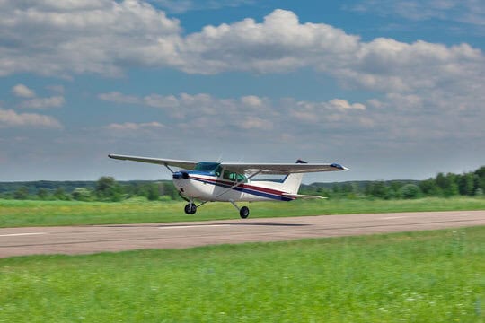 Small propeller plane landing on a runway with green grass and blue sky background.