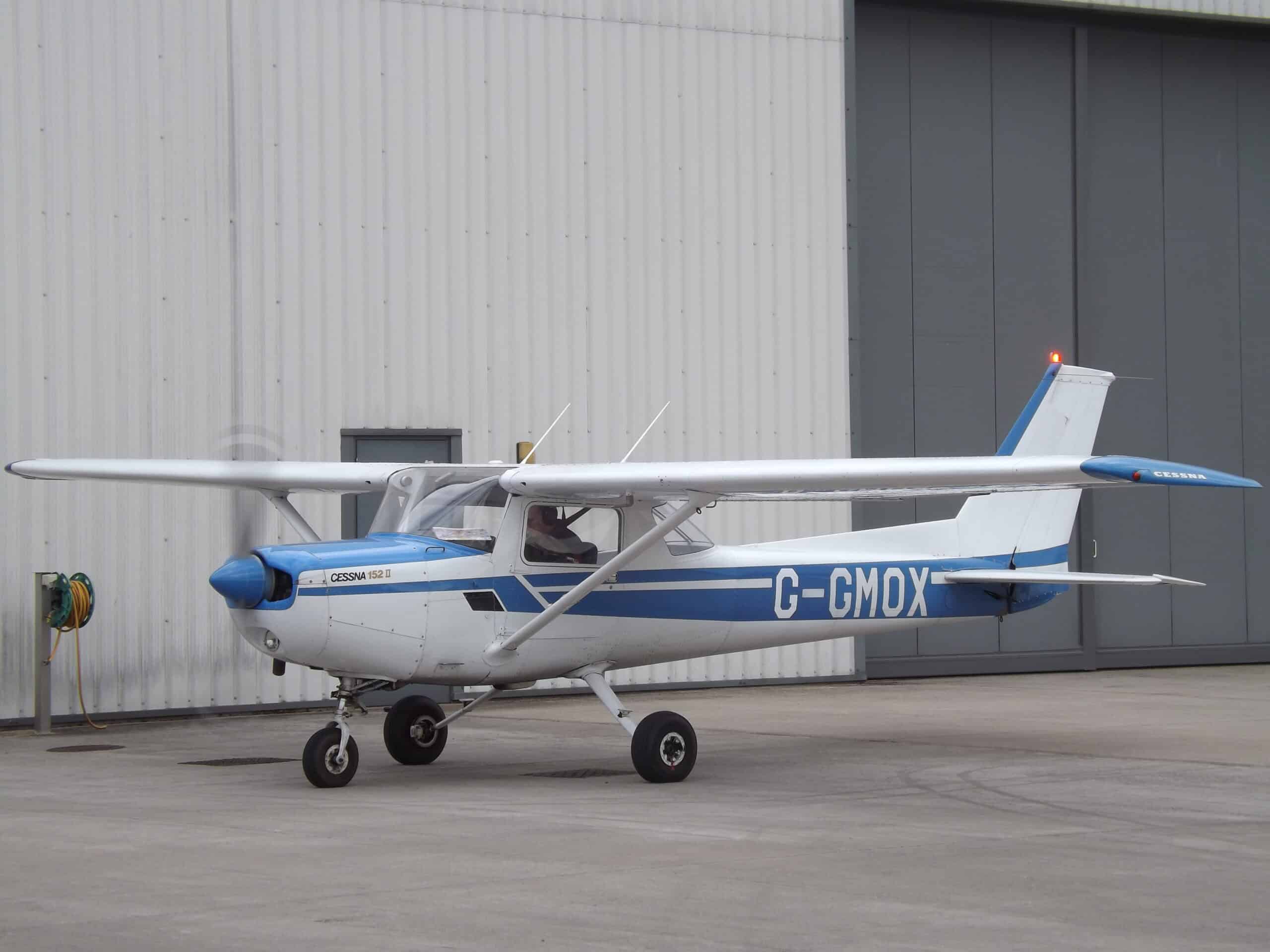 Small white and blue Cessna aircraft parked on tarmac at airport.
