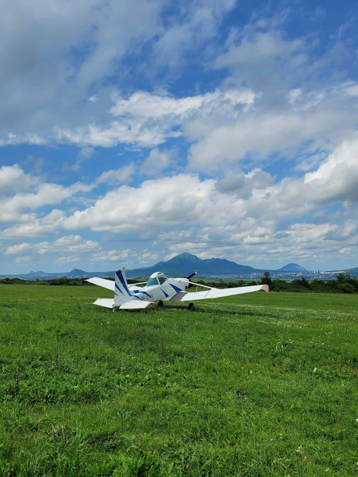 Aircraft on grassy airfield with mountains in background.