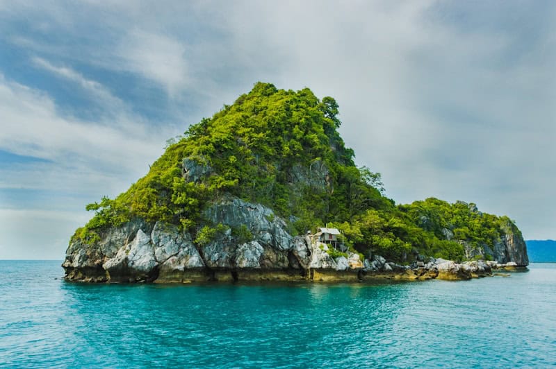 Island with lush greenery and rocky cliffs in turquoise ocean waters.