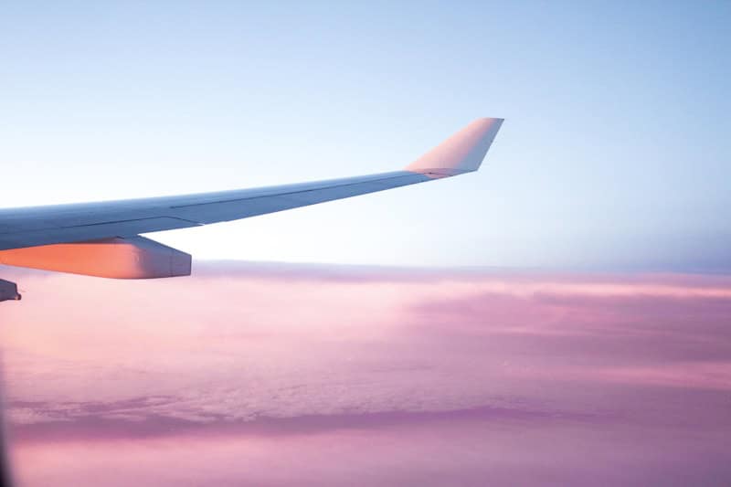 Aircraft wing in flight over a pink and blue sky at sunset.