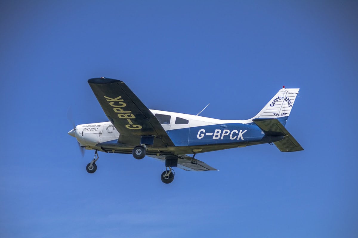 Small private aircraft flying in clear blue sky.
