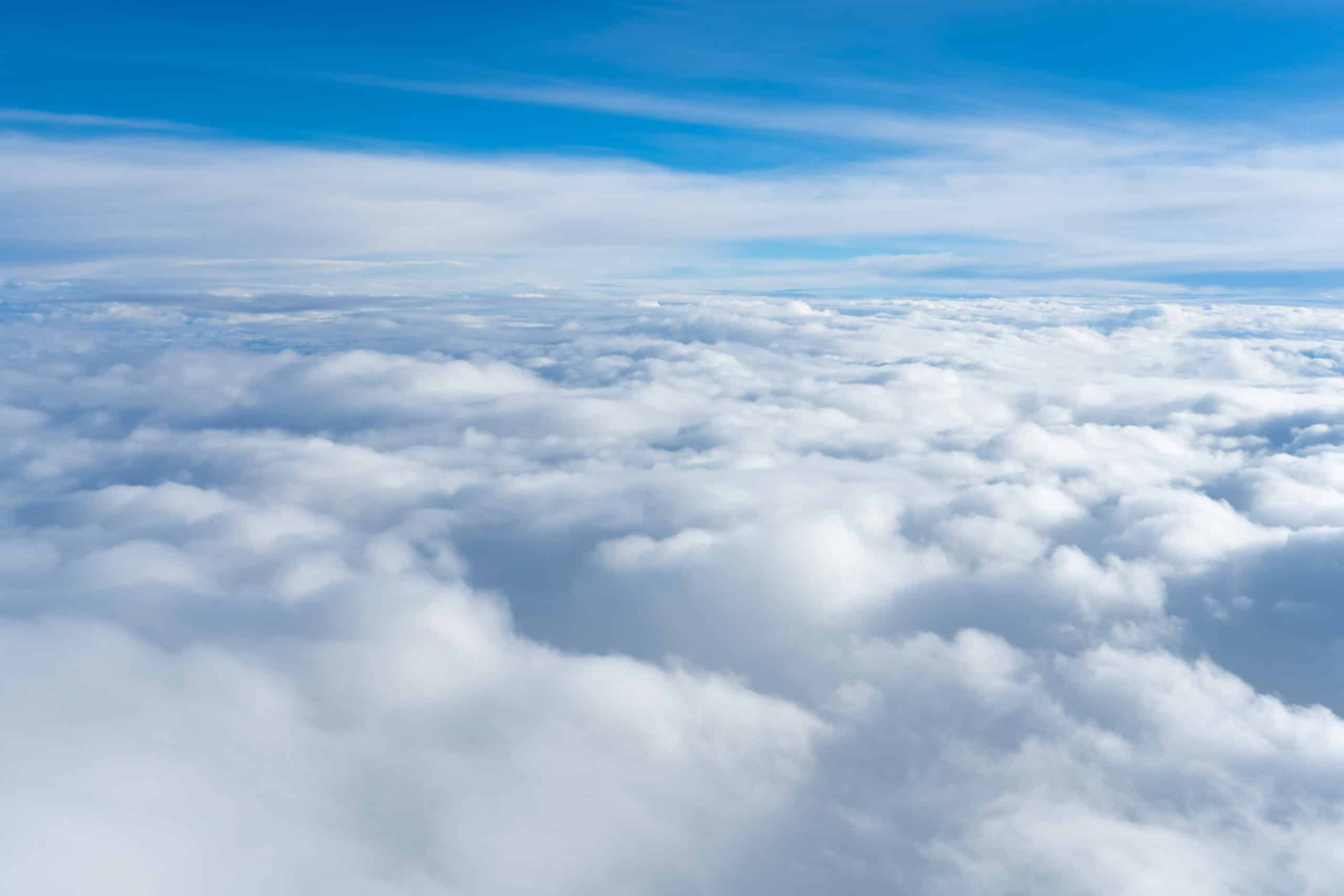 High-altitude view of clouds and blue sky from an airplane window.
