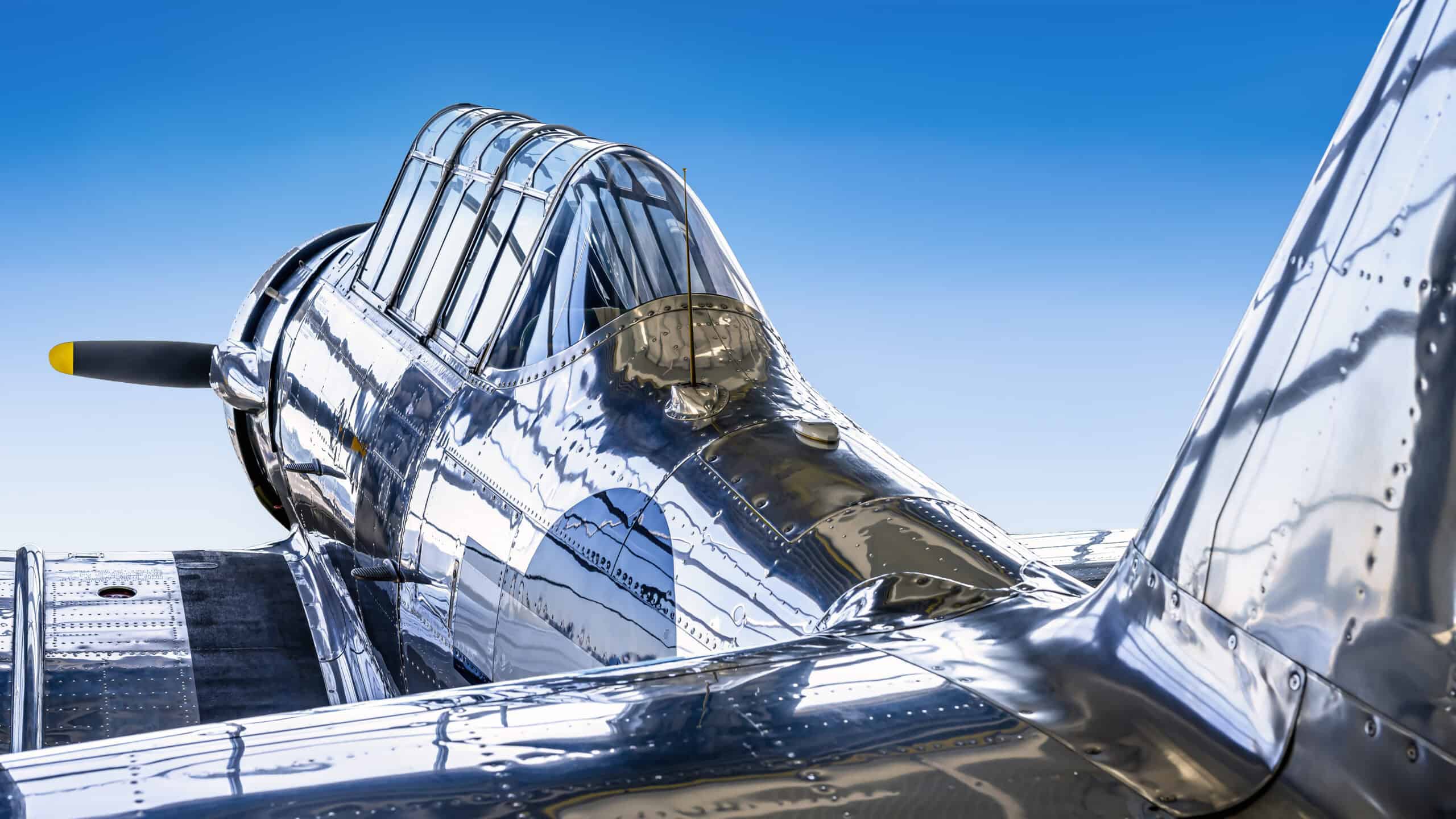 A sleek, shiny vintage aircraft with a glass cockpit and polished metal surface against a clear blue.
