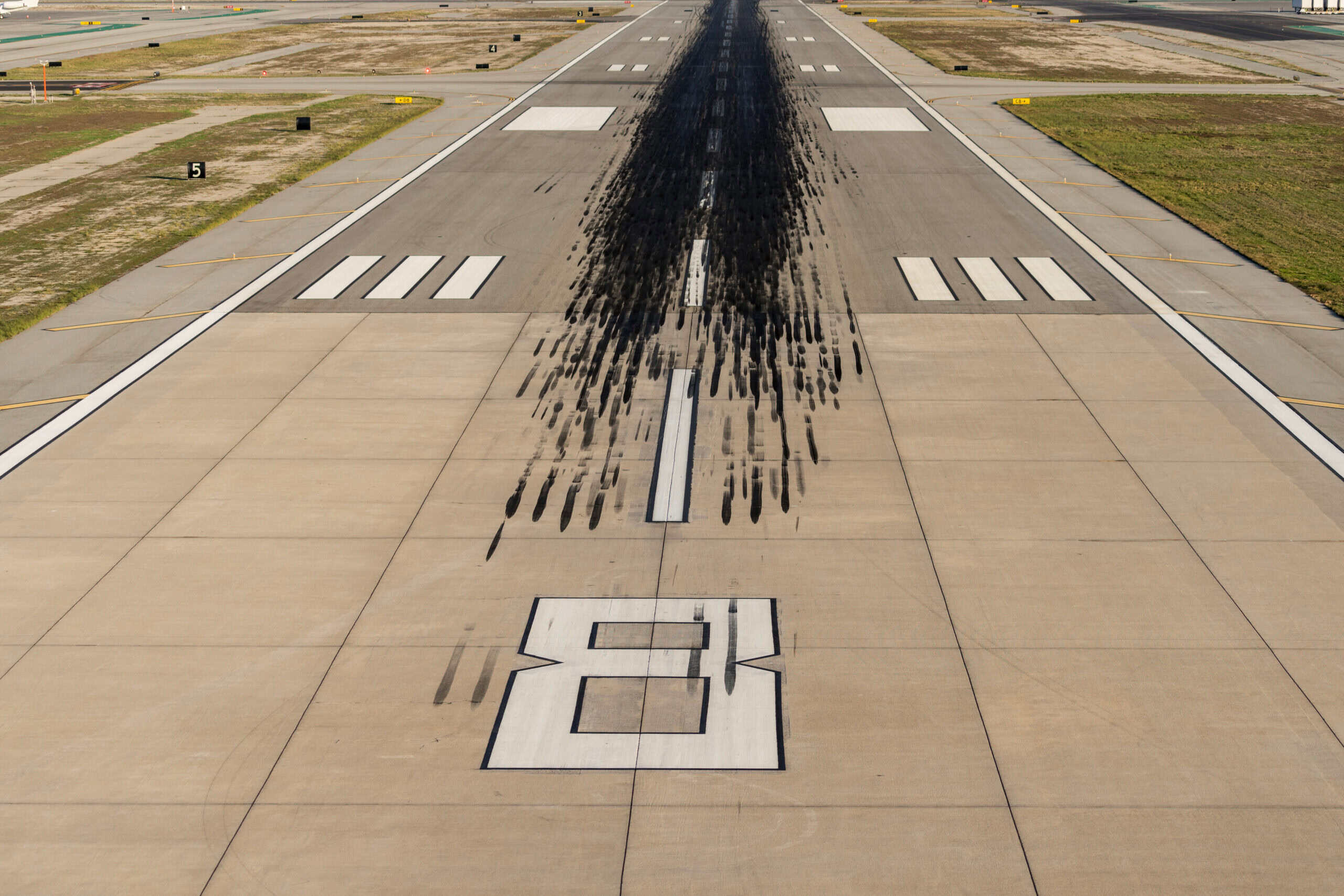 Runway with black tire marks at an airport, clear sky background.