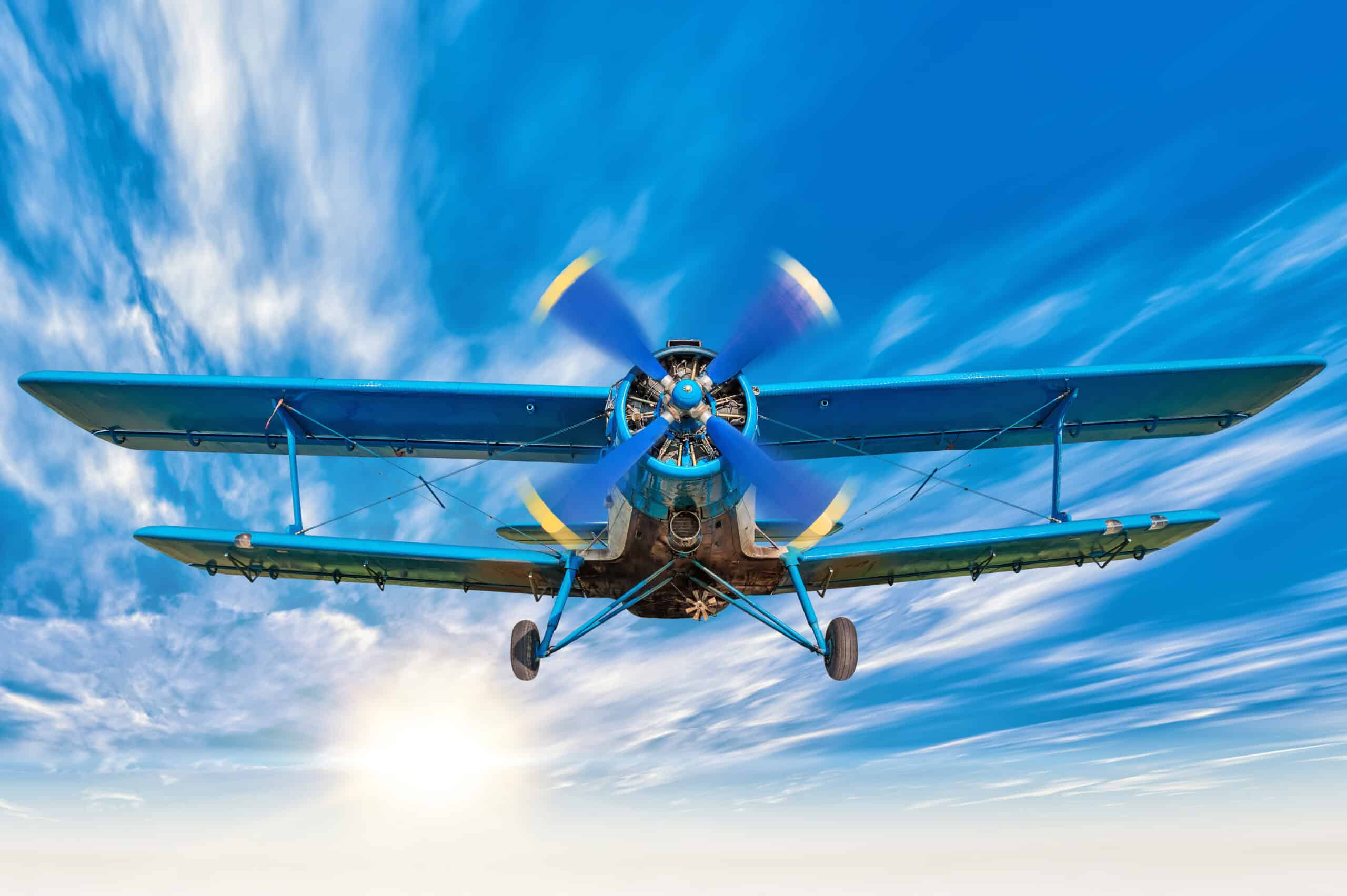 Blue radial-engine biplane in flight against clouds and sun
