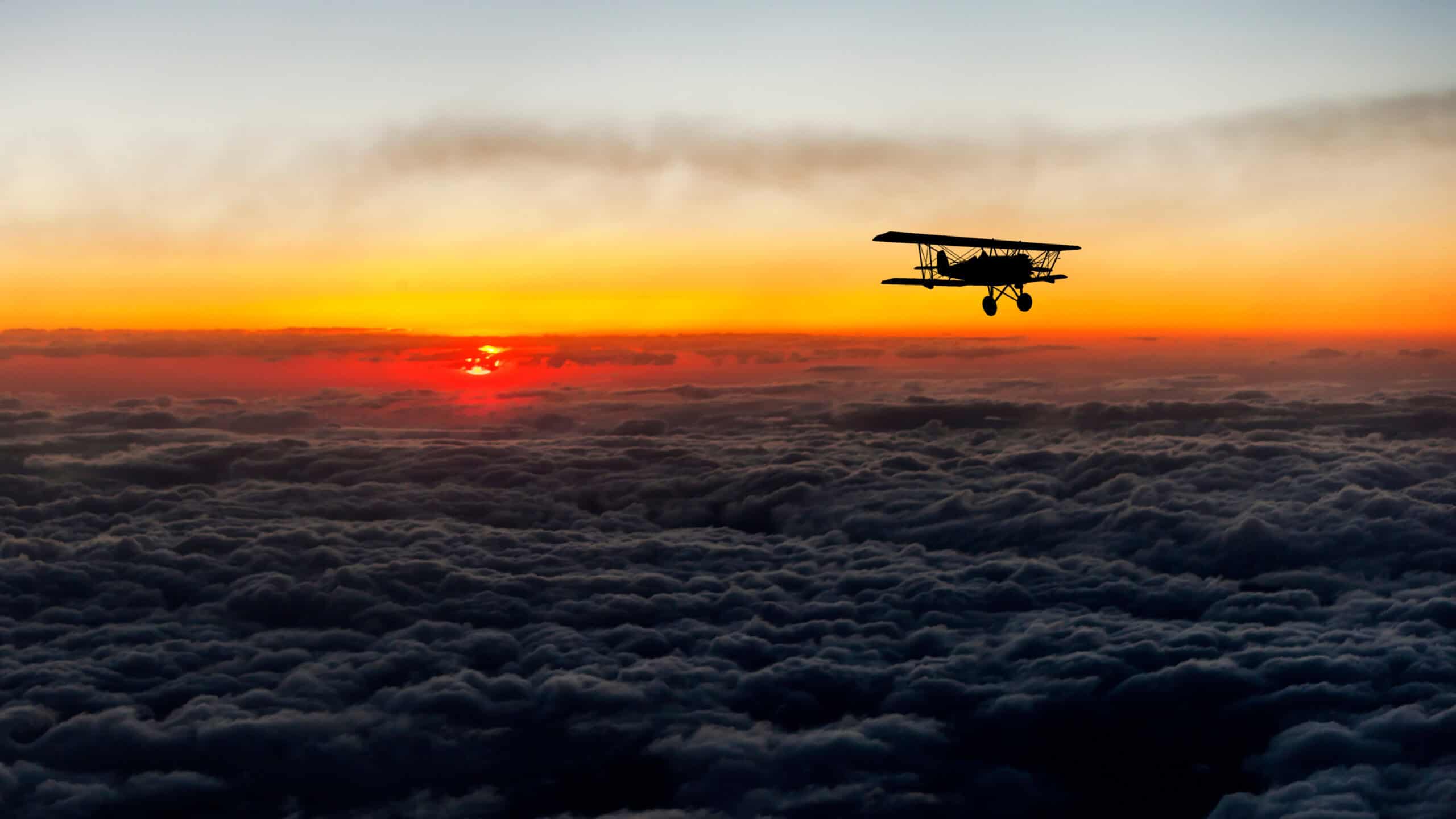 Biplane silhouette flying above clouds at sunset
