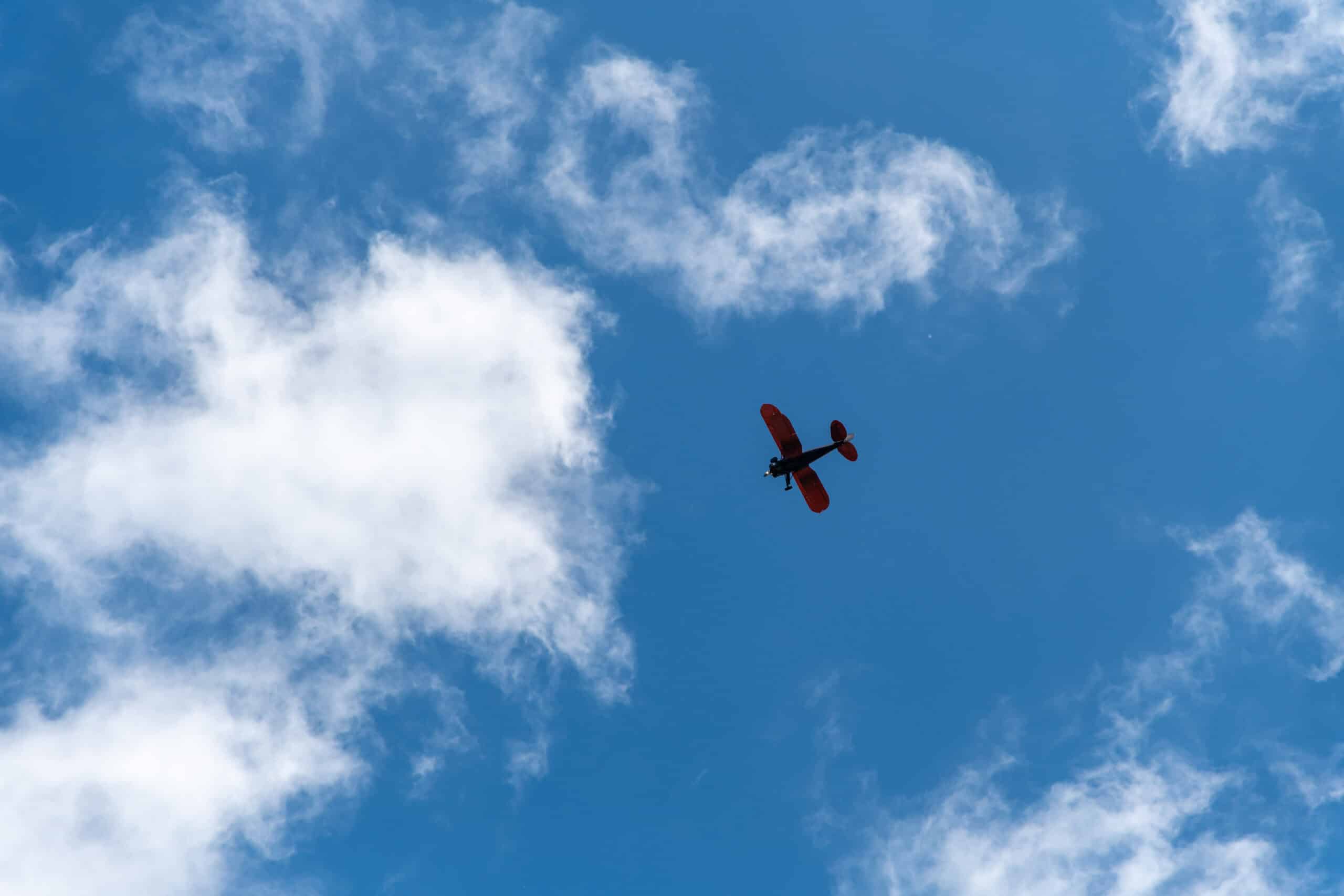 Biplane silhouetted against scattered clouds in blue sky