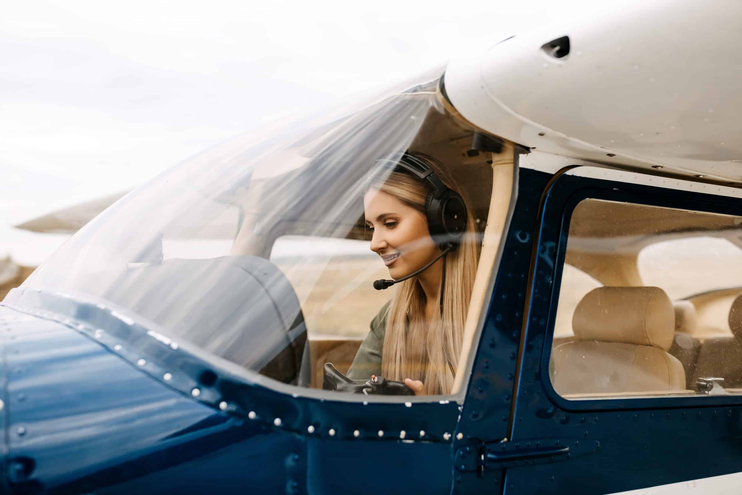 Female pilot with headset inside small aircraft cockpit preparing for flight.