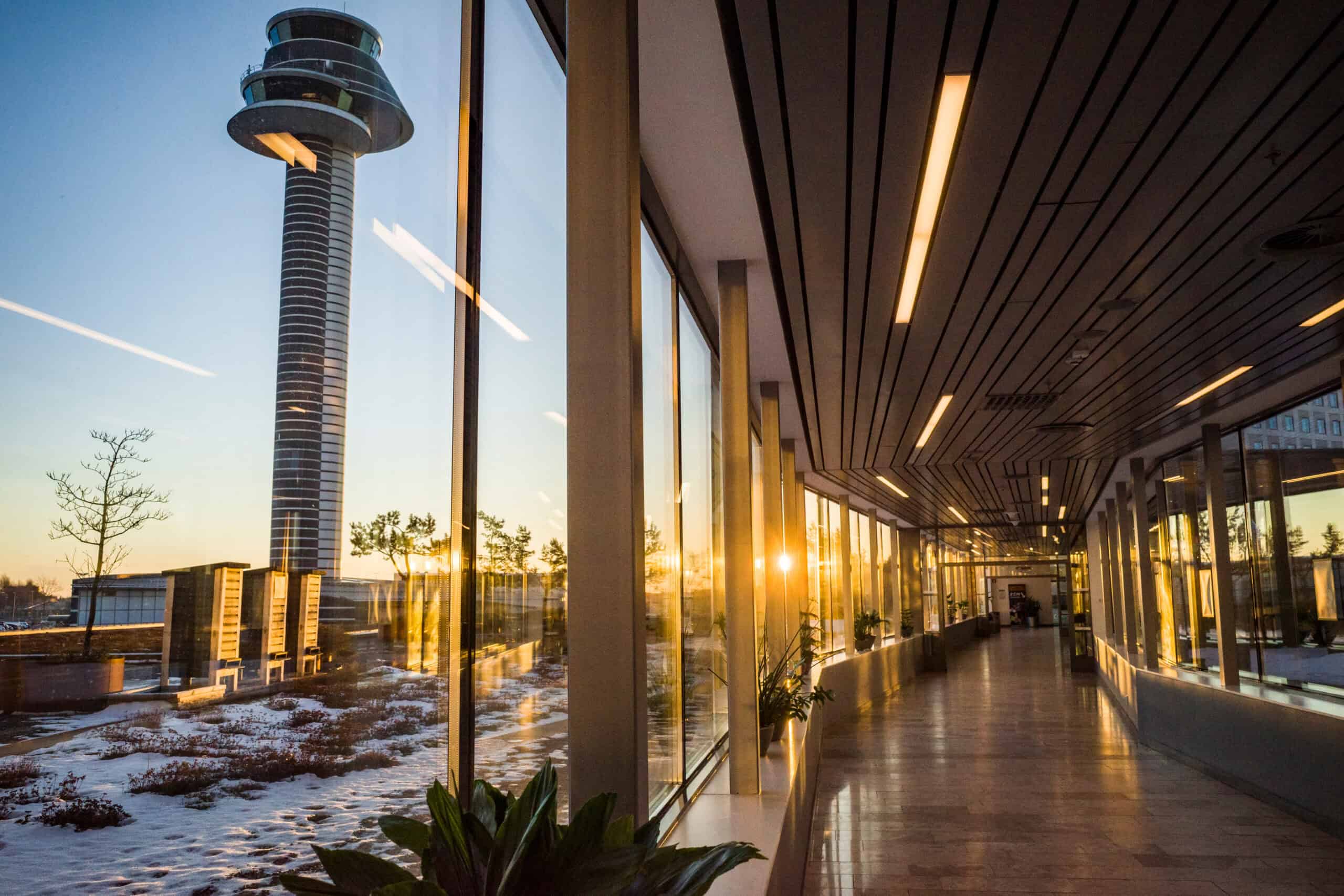 Modern airport terminal interior with large glass windows and city view at sunset.