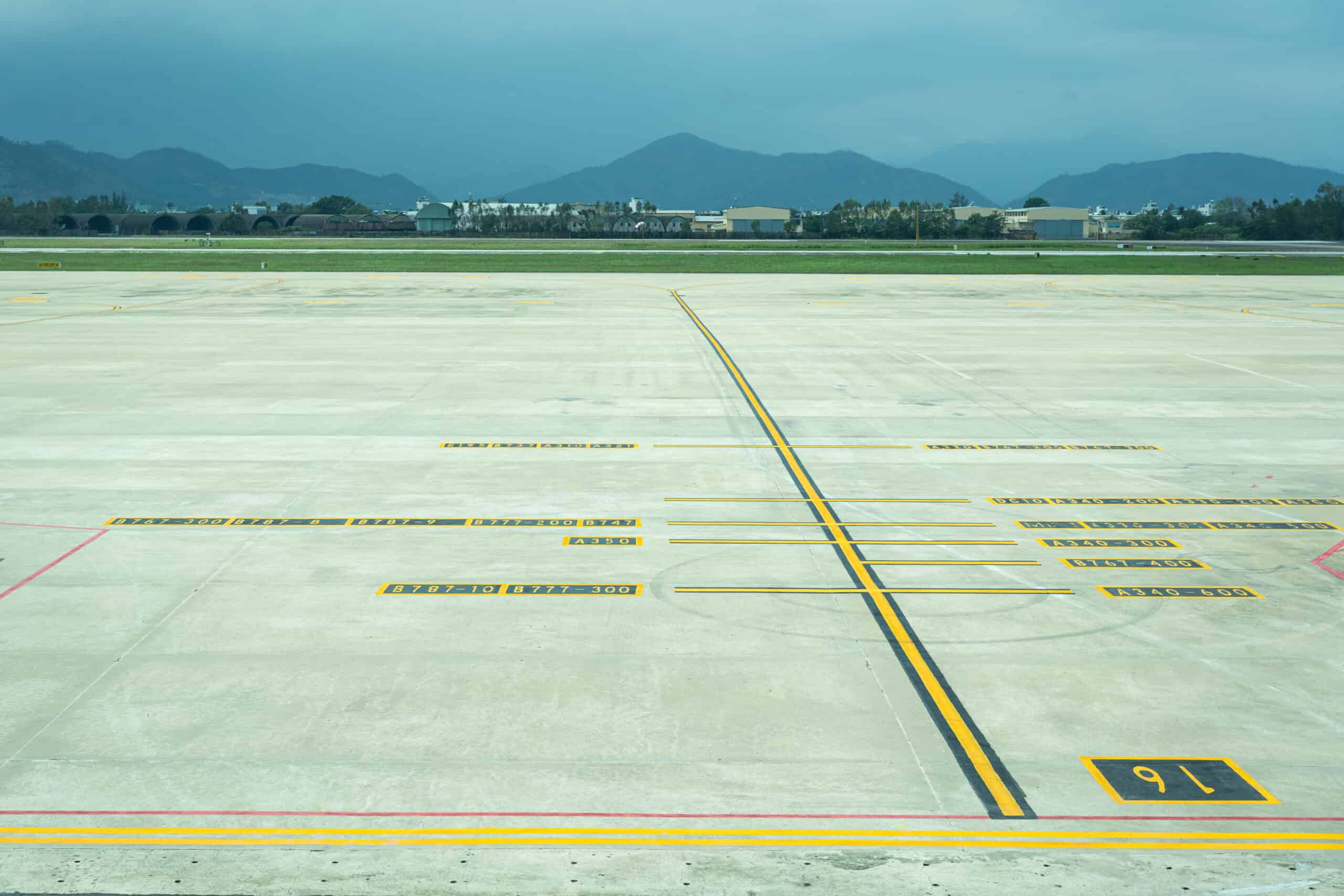 Airport tarmac with marked parking positions and runway numbers under cloudy sky.