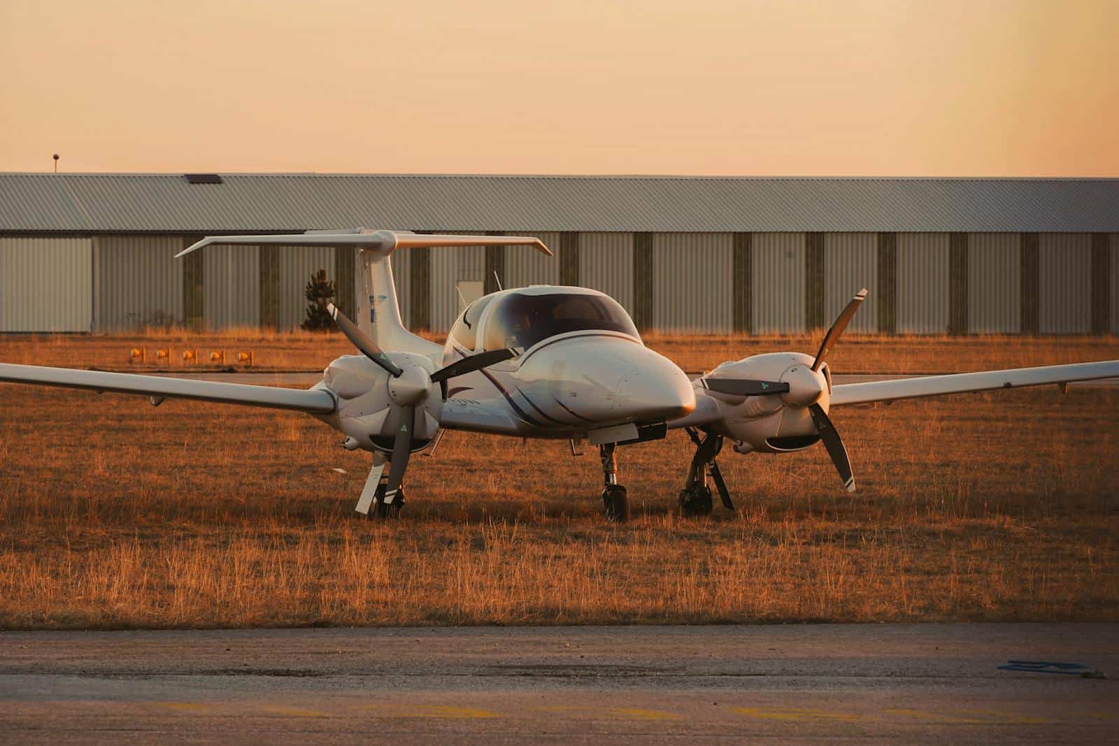 Private aircraft parked on grass near a hangar at sunset