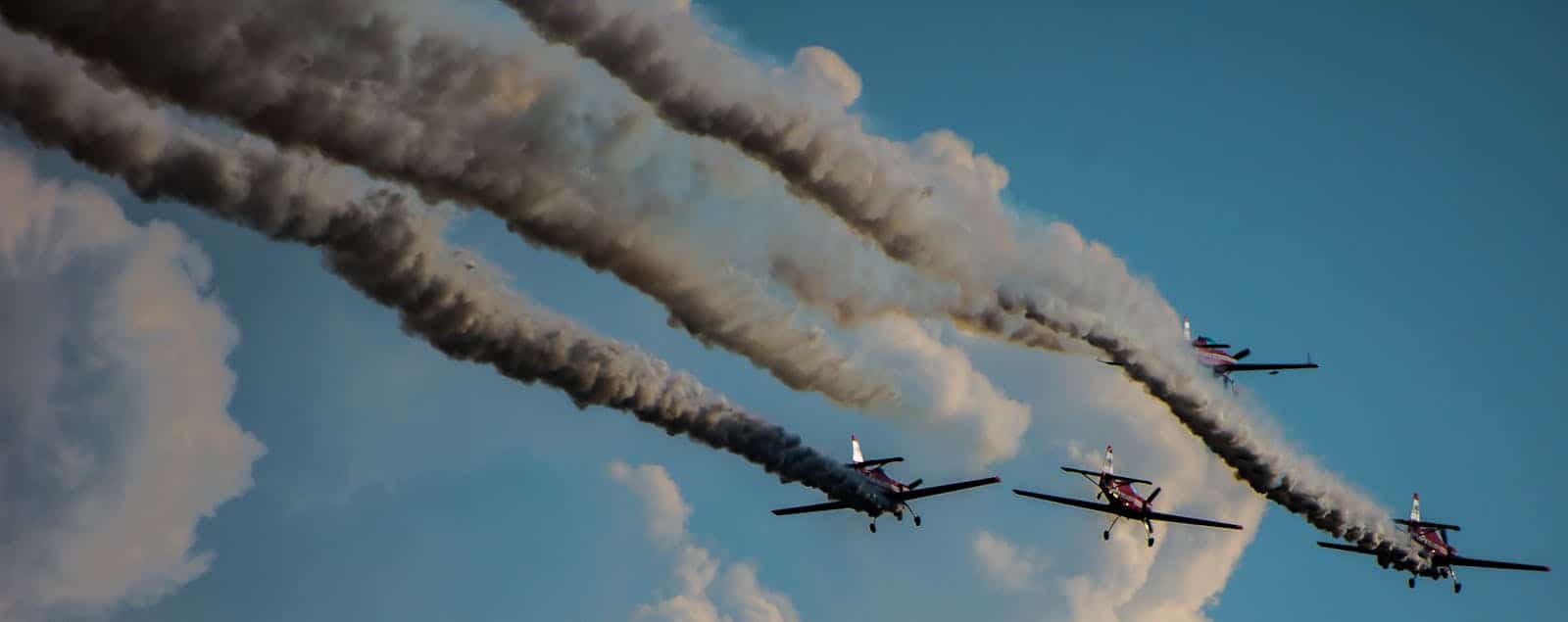 Four stunt aircraft performing aerobatic maneuvers with smoke trails