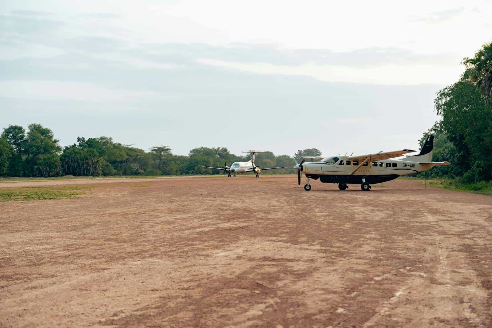 Aircraft parked on a dirt runway at a small airfield with trees in the background.