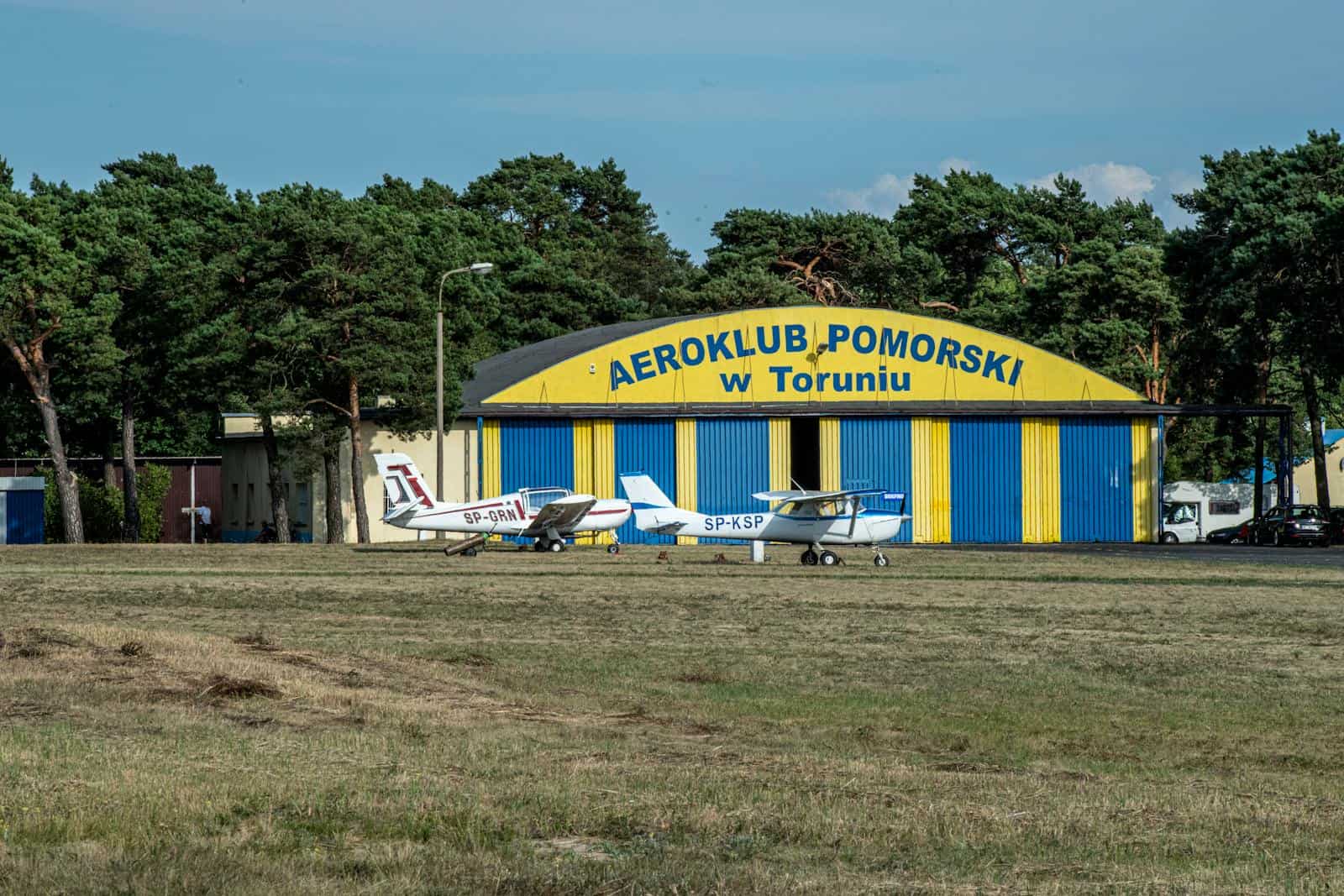 Two small planes parked at an aero club hangar