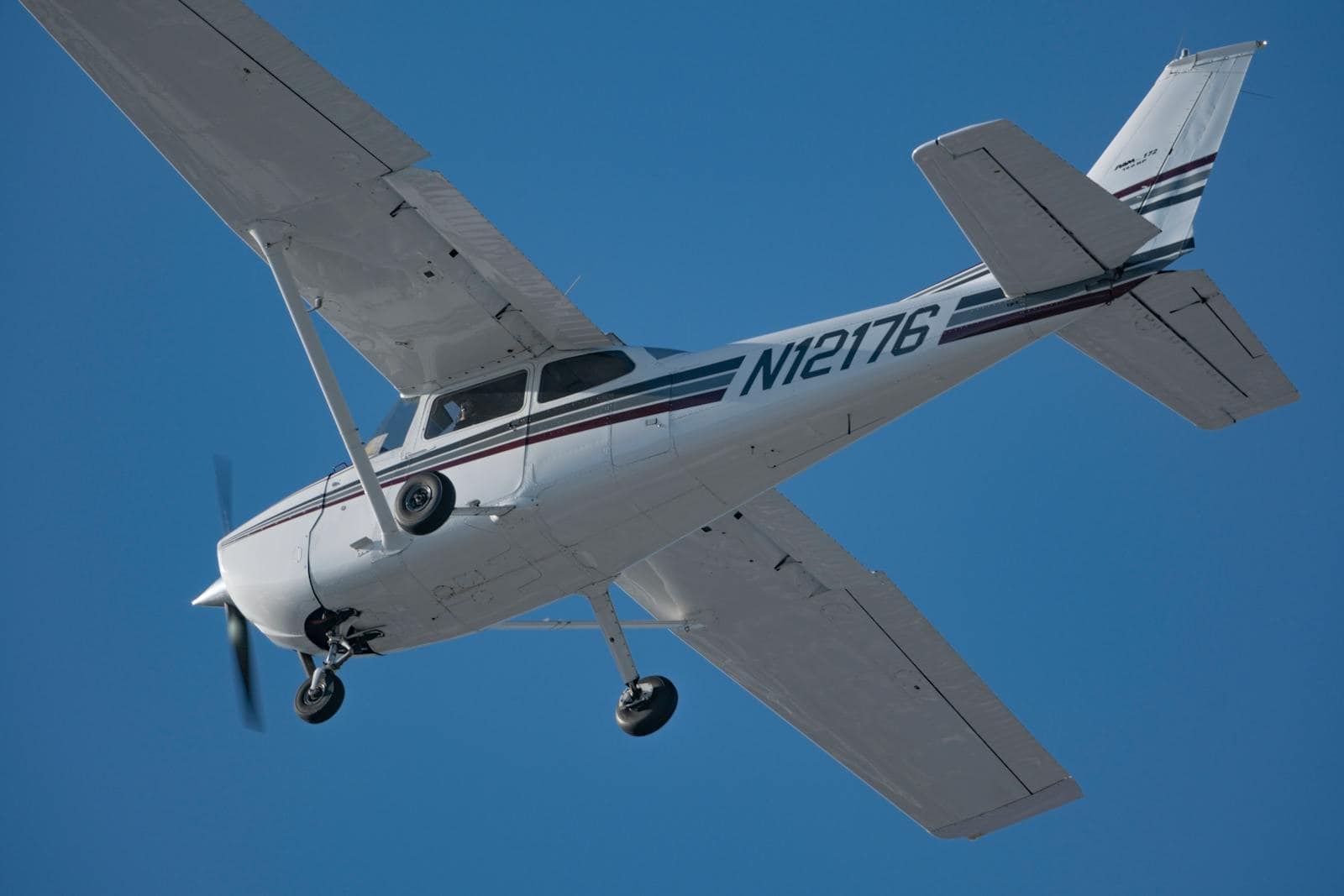 Private aircraft in flight with landing gear extended, soaring through a clear blue sky.