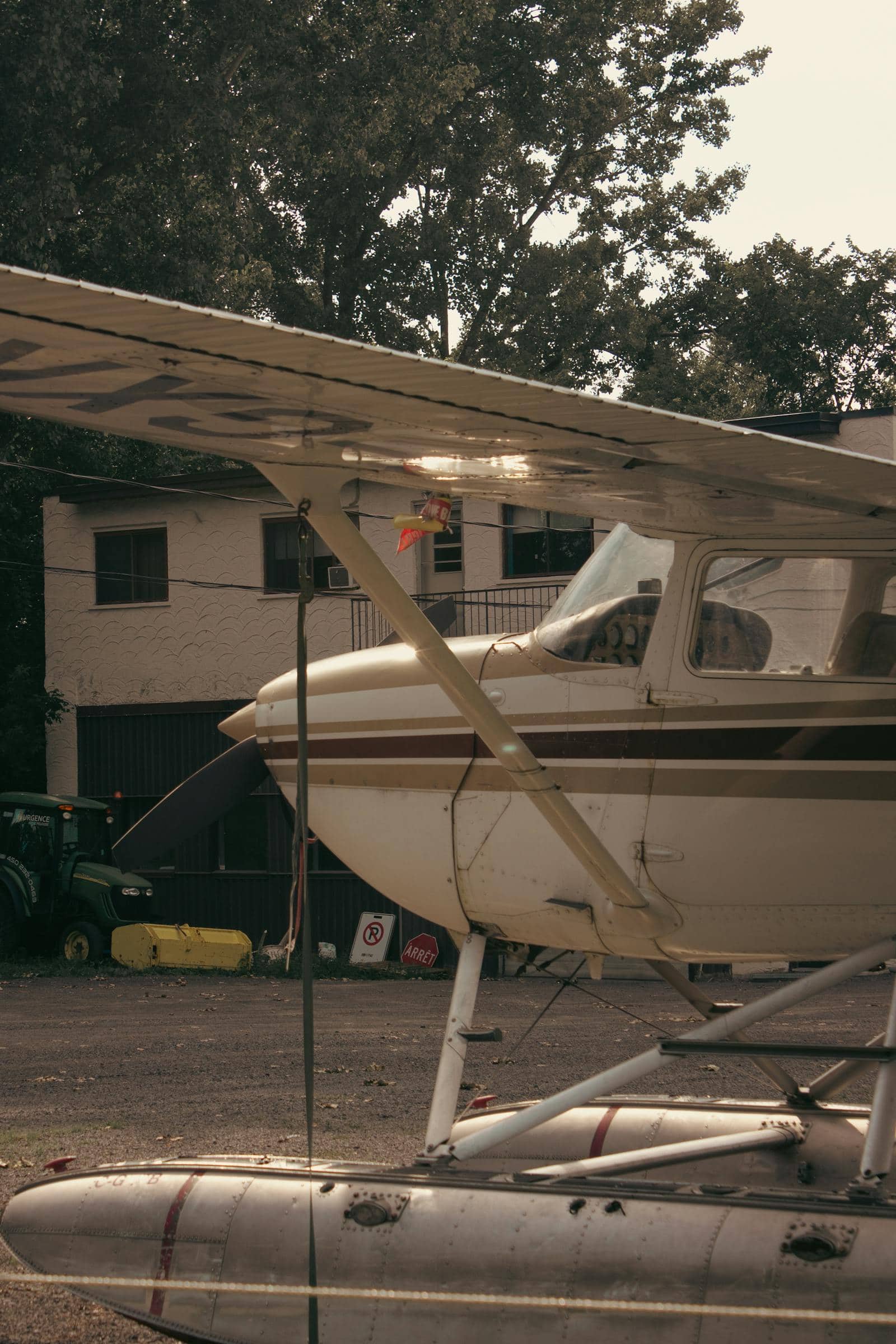 Small Cessna airplane parked on the tarmac with trees and buildings in the background.
