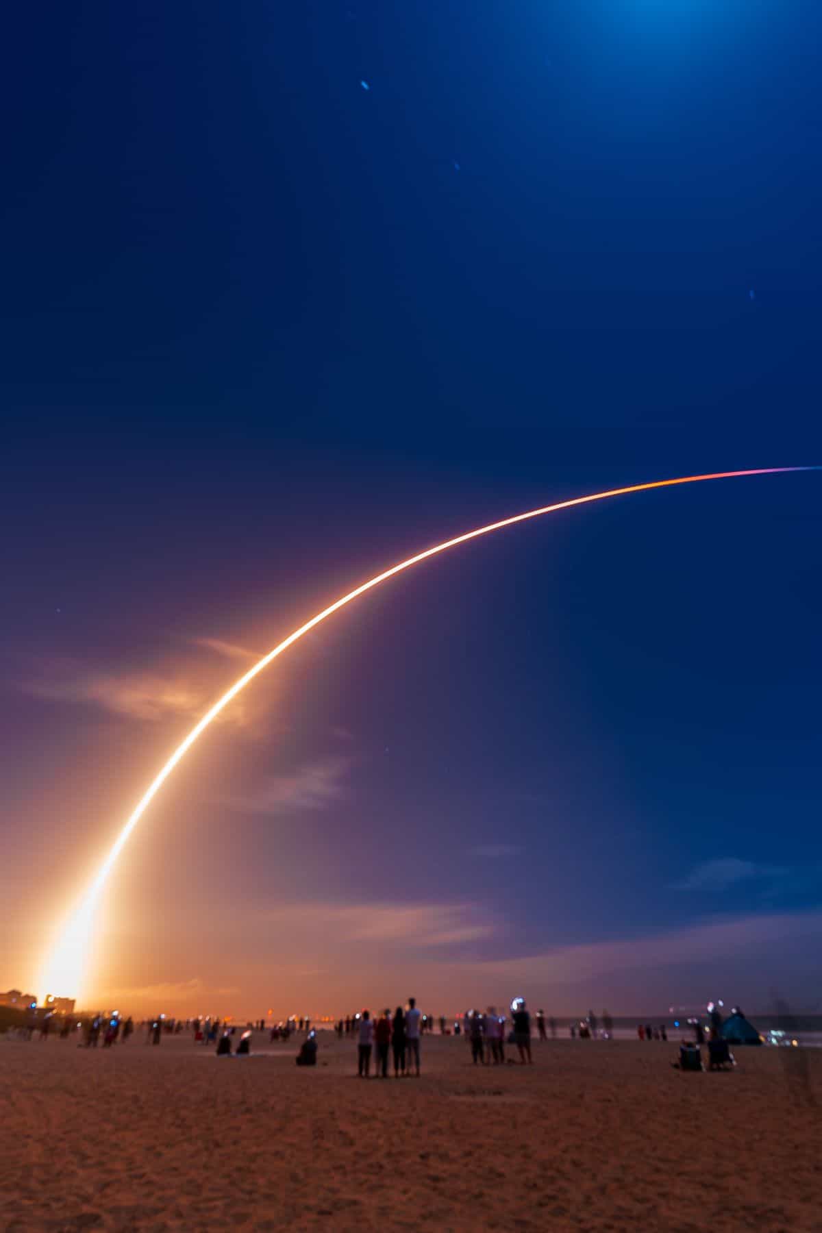 Rocket launch at night with spectators on the beach.