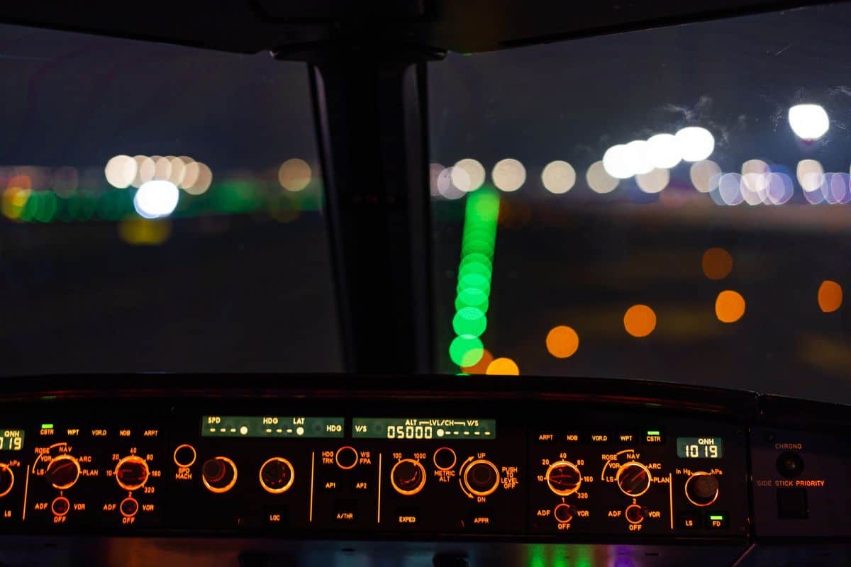 Aircraft cockpit night view with illuminated controls and blurred runway lights.