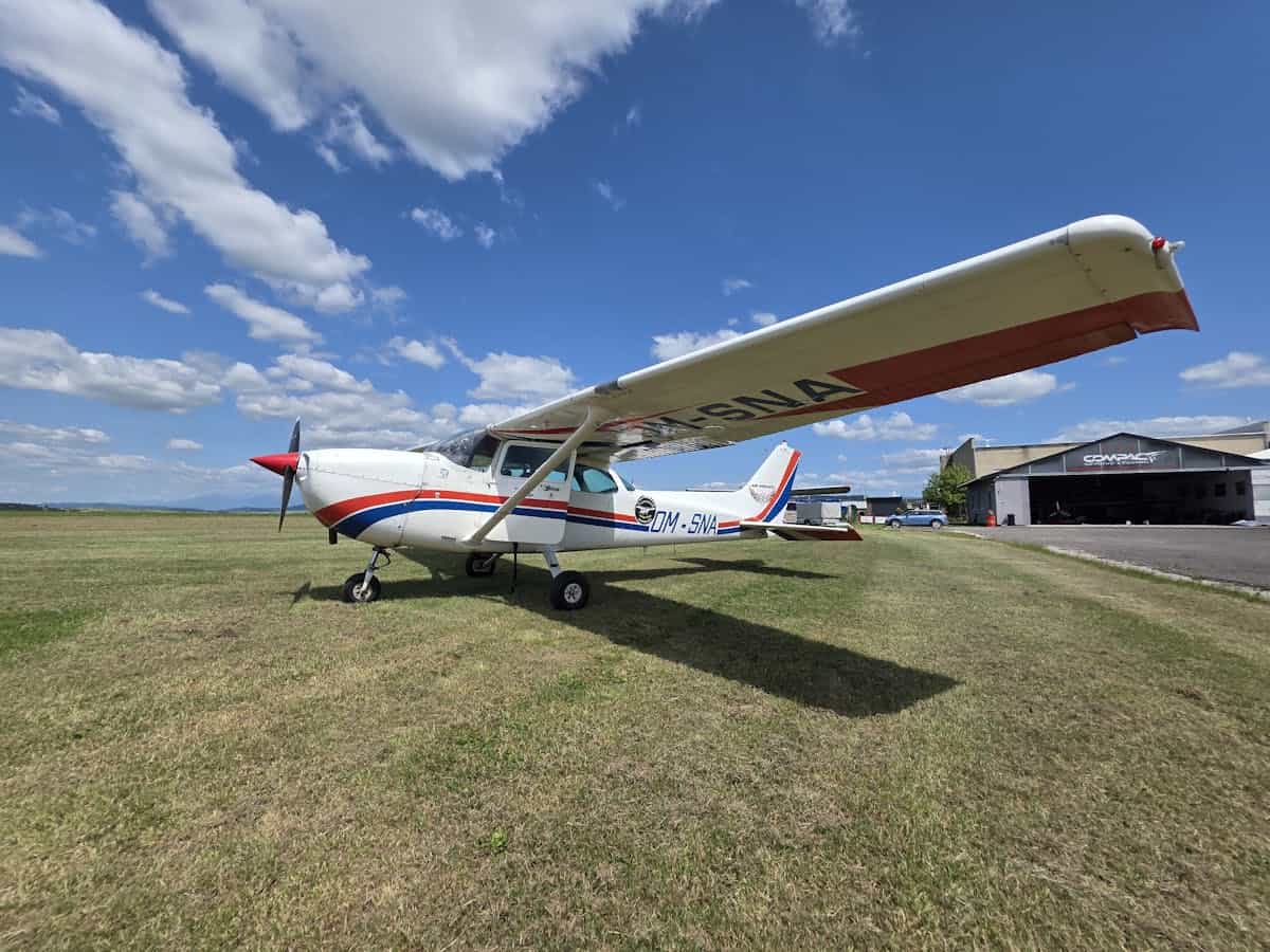 Small aircraft parked on a grassy airfield with hangar in background