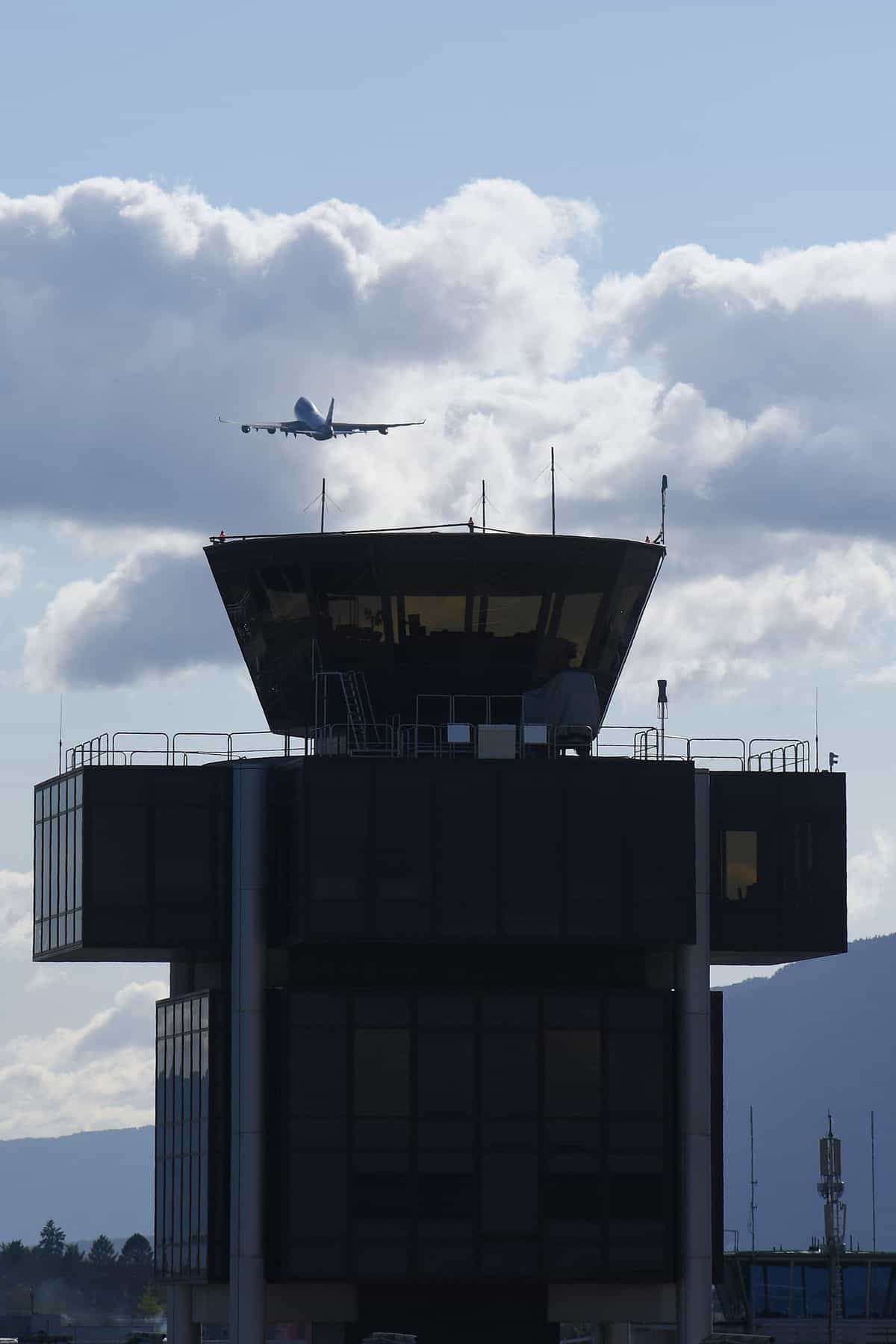 Commercial airplane approaching airport with control tower in foreground.