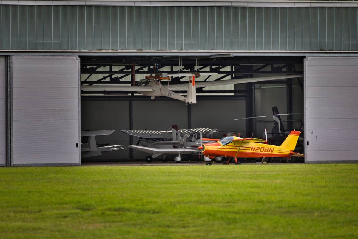 Yellow private aircraft parked outside a hangar on a sunny day