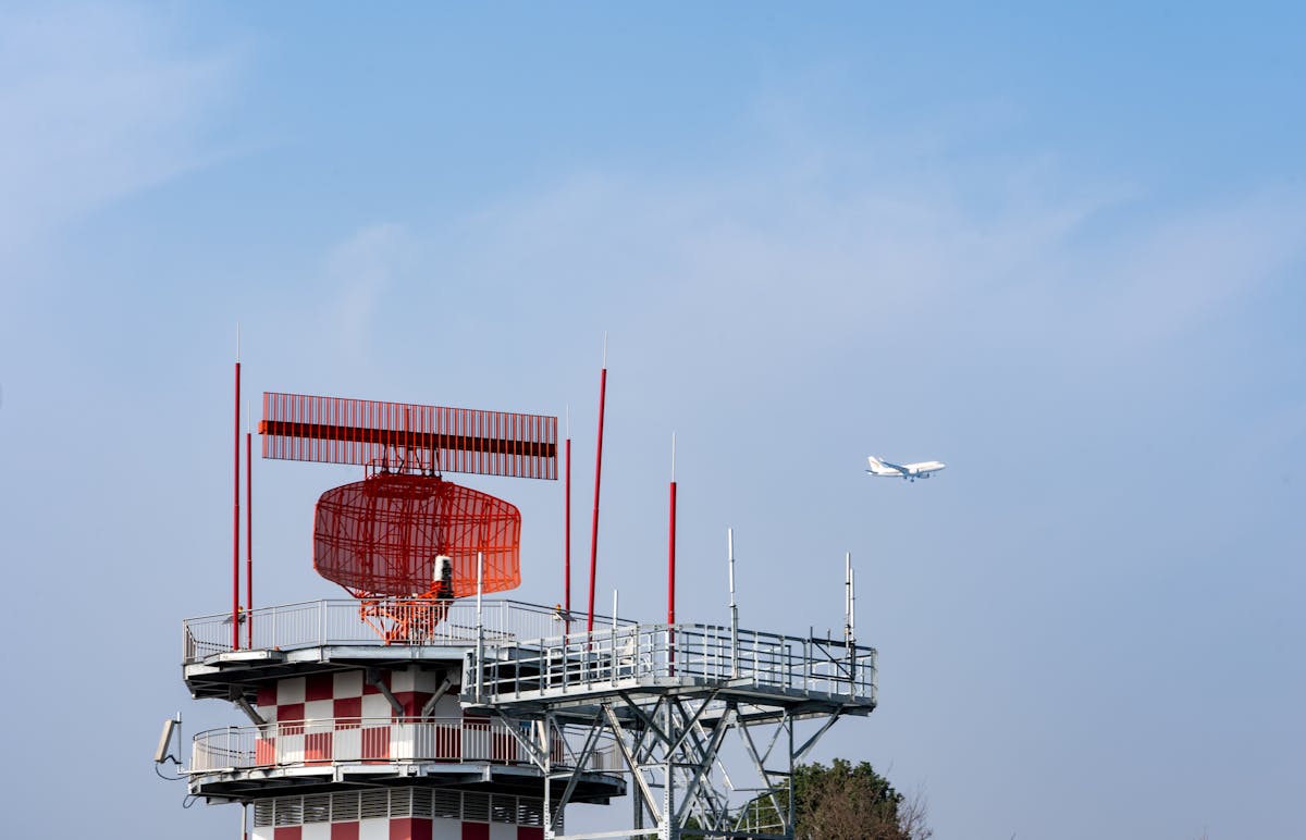 Control tower with radar and communication equipment, aircraft flying in the background under a clea.