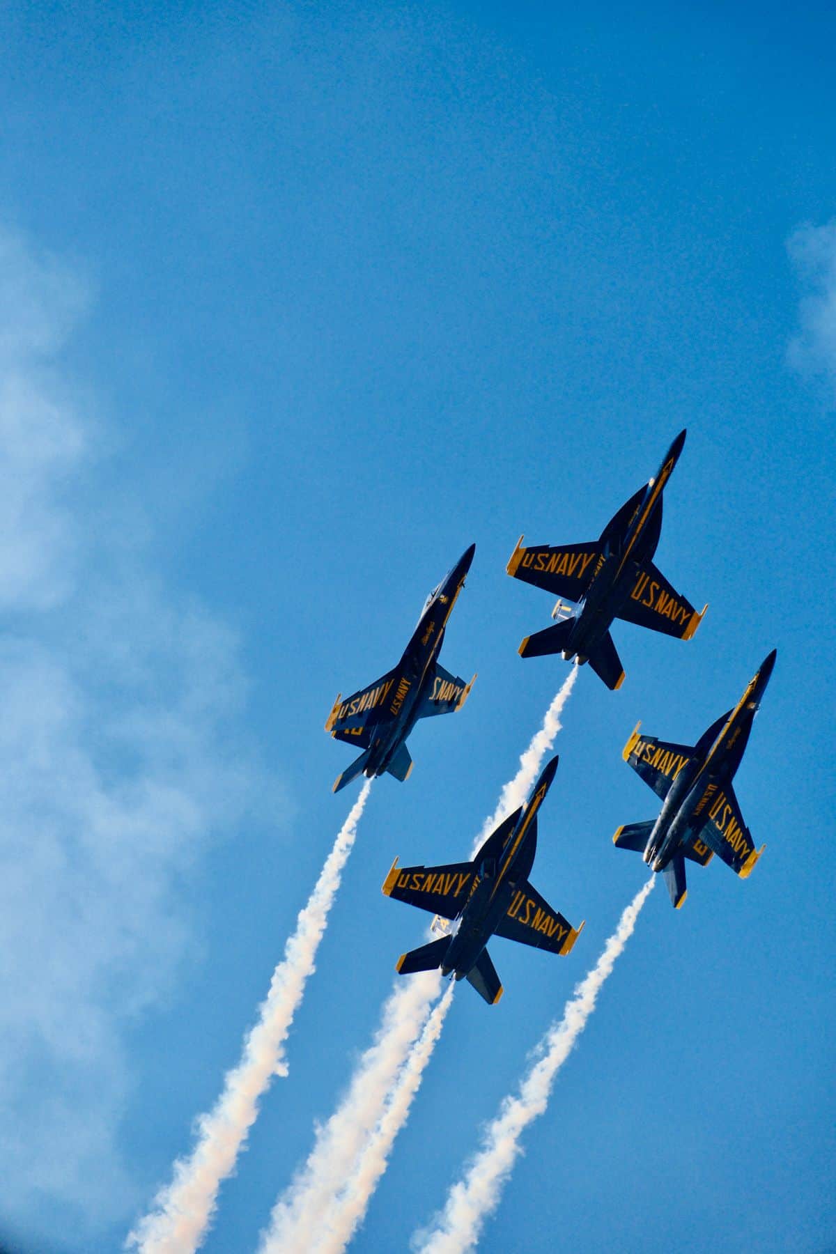 Four US Navy Blue Angels jets performing a synchronized flyby with smoke trails.