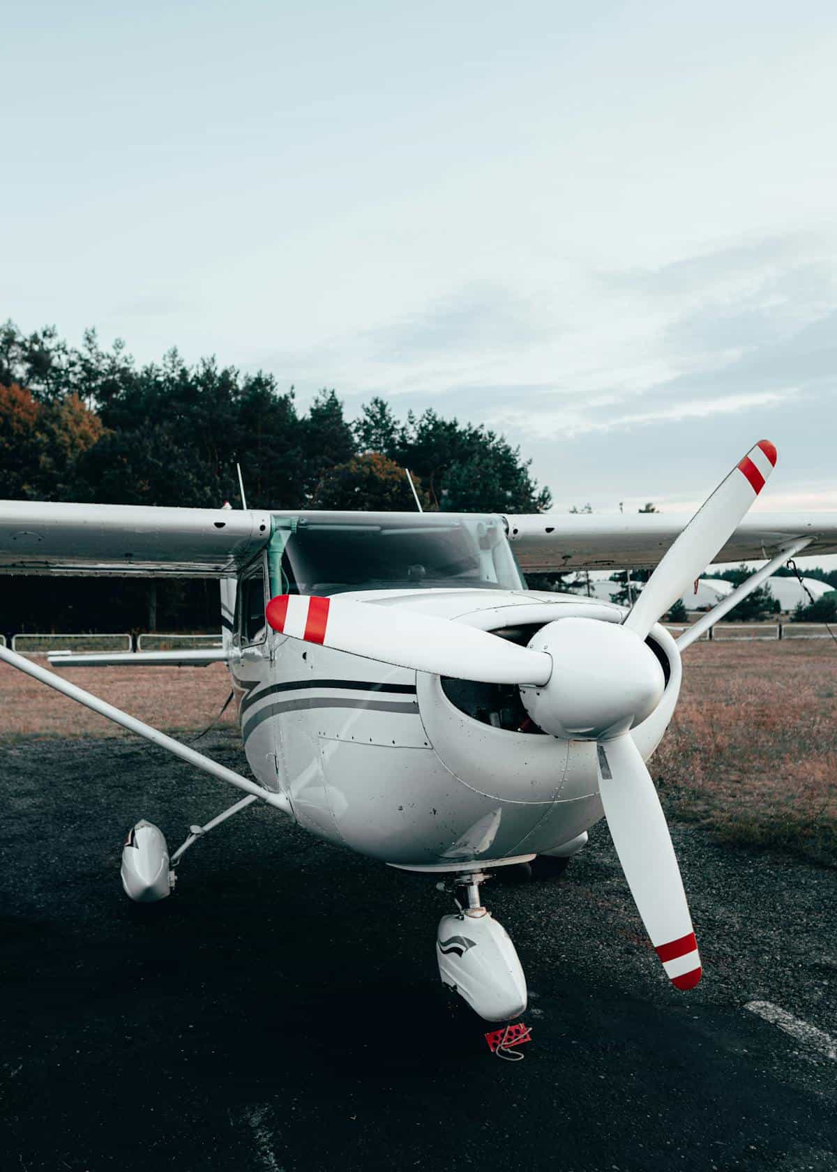 Small white single-engine aircraft parked on runway with propeller and tailwheel.