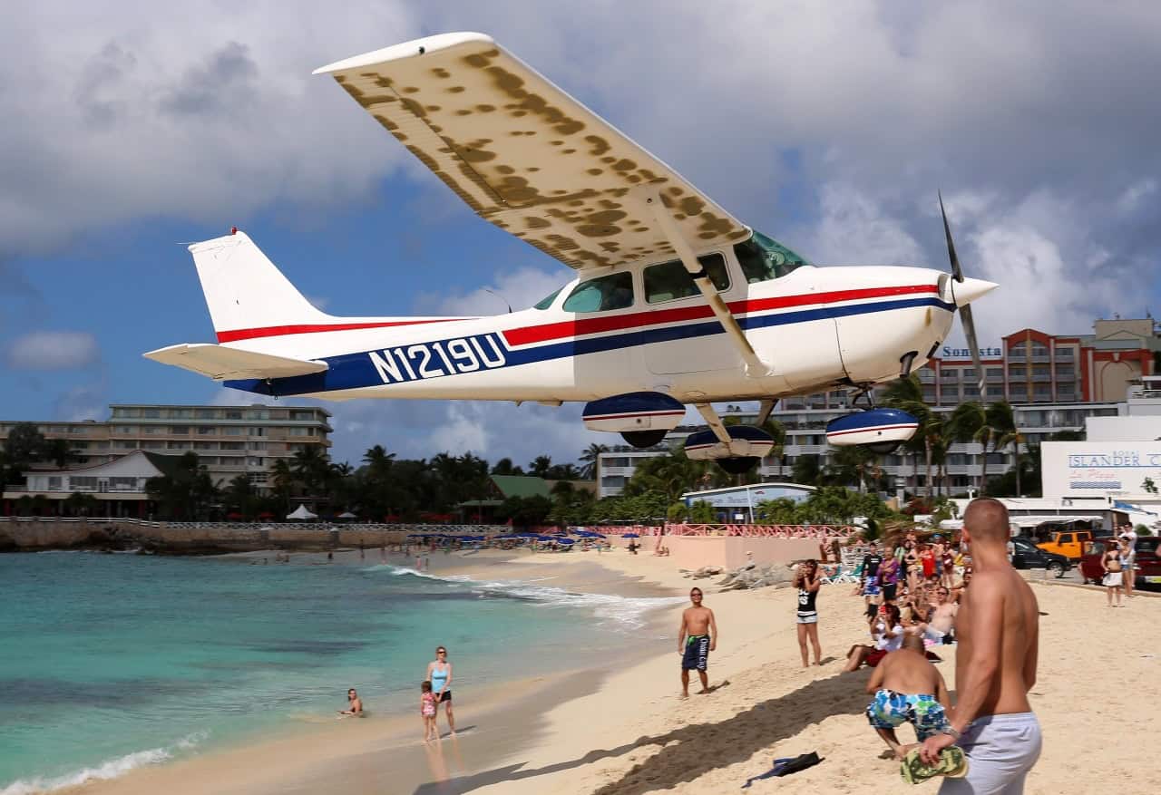 Seaplane landing on beach with people and buildings nearby.