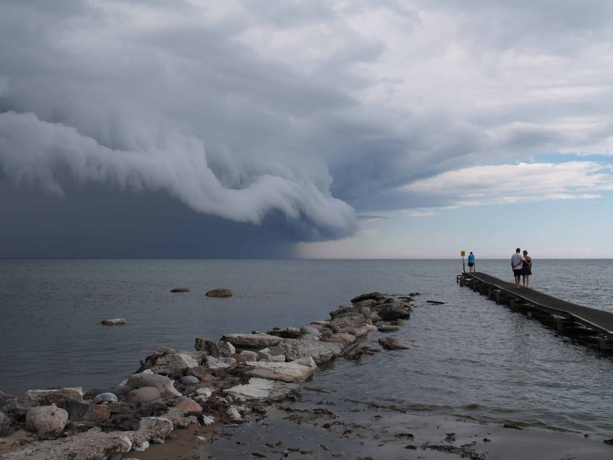 Storm approaching over the lake with people on a pier observing.