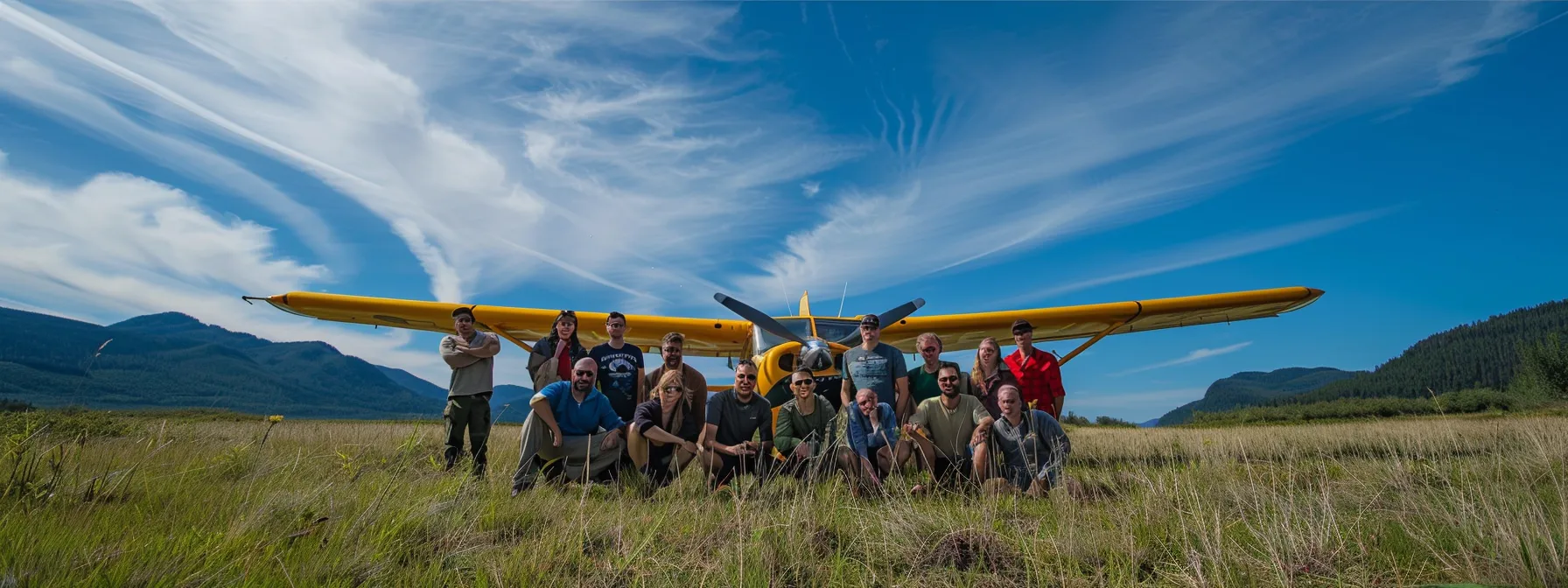 A diverse group of smiling pilots and aviation enthusiasts gather around a vibrant bush plane at a sunny grass airfield.