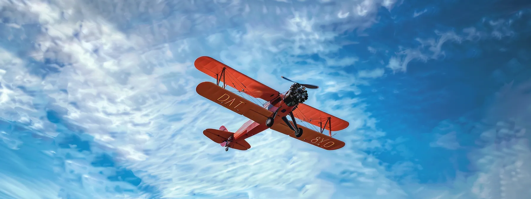 a majestic vintage biplane soars through a clear blue sky, its vibrant colors contrasting beautifully with delicate wisps of white clouds, capturing the spirit of aviation in a breathtaking display of freedom and nostalgia.